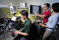 Georgia Tech graduate students Kwanghun Chung and Matthew Crane, and assistant professor Hang Lu (left to right), set up the microchip on the microscope and observe a live image of it on the monitor. (Georgia Tech Photo: Gary Meek) 